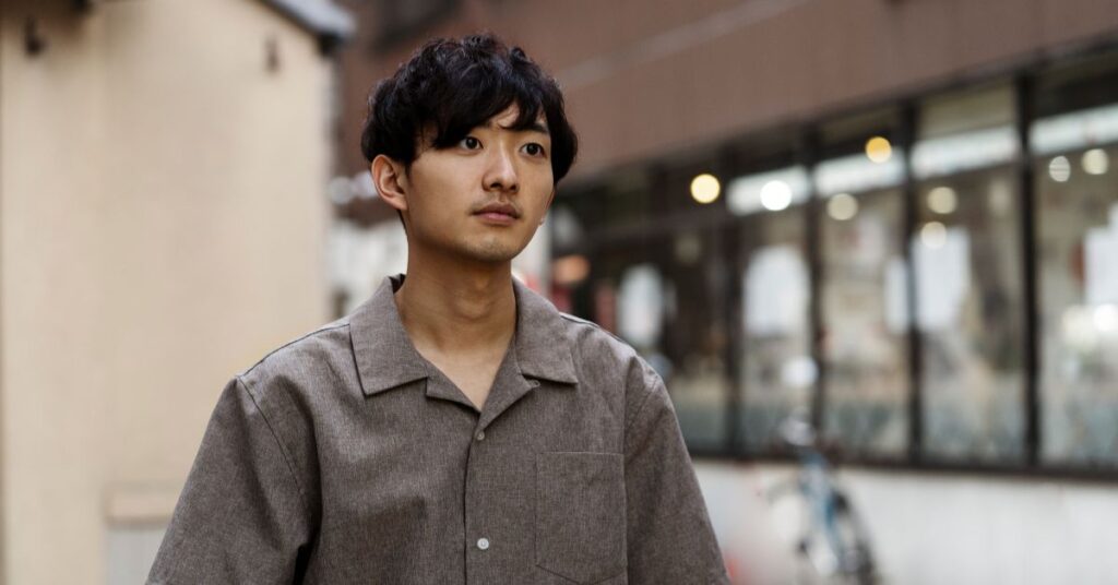 Korean shaggy cut for men featuring soft S-shaped waves, a light airy texture, and a long face-framing fringe.