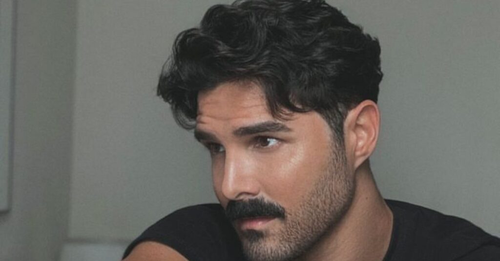 Natural wavy hair on top with a clean mid fade.